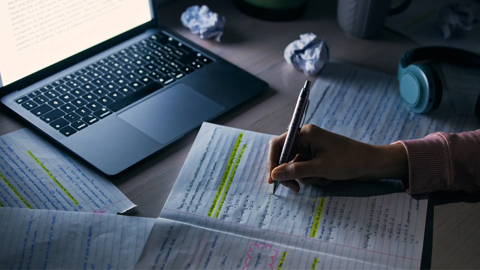 Writing notes by hand beside a laptop while preparing a manuscript